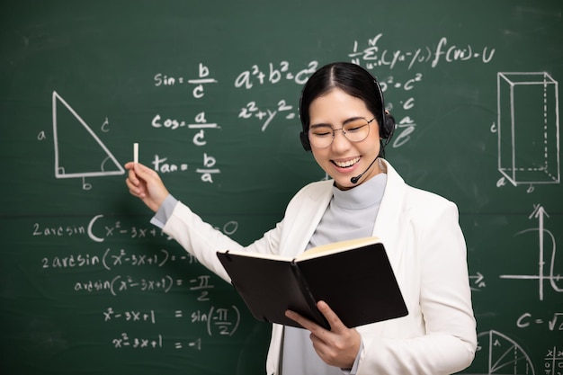 Young asian teacher woman teaching holding book and chalk video conference with student looking camera Female teacher training the mathematics in classroom blackboard from online course