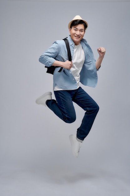 Young Asian tourist backpacker man smiling and jumping isolated on white background