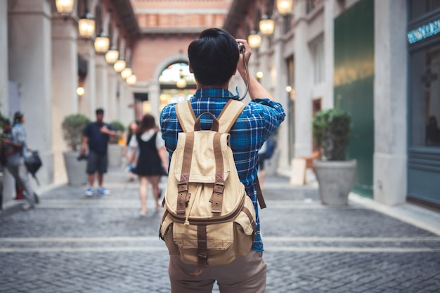 Young Asian traveling backpacker in street city and walking with take a photo and camera