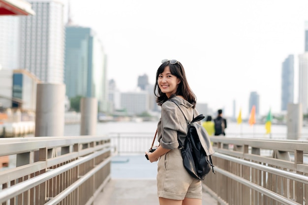 Young Asian woman backpack traveler waiting an express boat at pier on Chao Phraya River in Bangkok