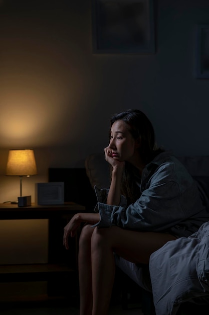 Young Asian woman in bedroom feeling sad tired and worried suffering depression in mental health woman sitting in bed cannot sleep from insomnia