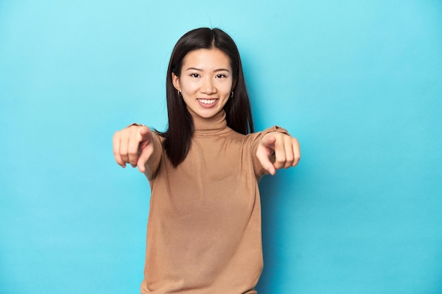 Young Asian woman in brown turtleneck cheerful smiles pointing to front