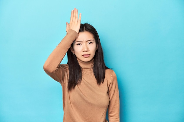 Young Asian woman in brown turtleneck forgetting something slapping forehead with palm