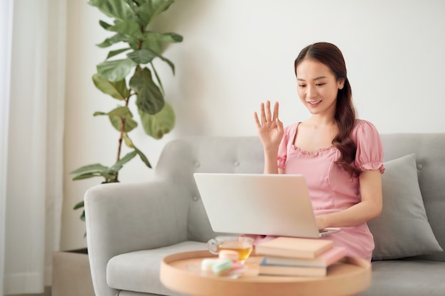 Young Asian woman calling her friend by laptop at living room.