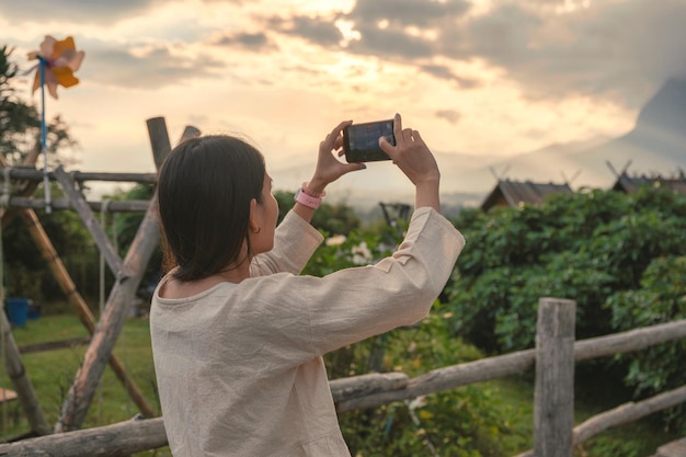 Young asian woman in casual cloth taking a photo with smartphone on hill in tropical rainforest