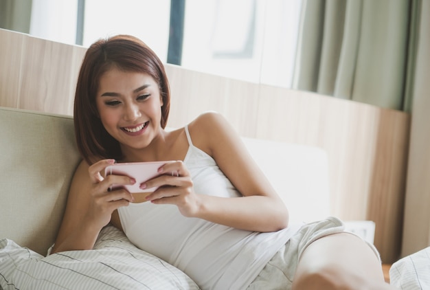 Young asian woman checking her smart phone lying in bed