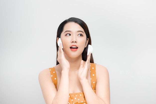 Young asian woman cleaning beauty face, using cotton pads, cleansing lotion and facial toner for removing makeup.