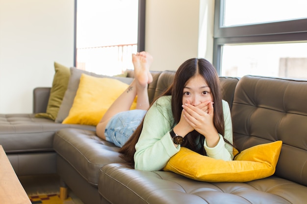 Young asian woman covering mouth with hands with a shocked, surprised expression, keeping a secret or saying oops