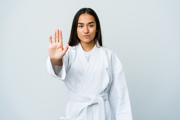 Young asian woman doing karate isolated on white wall standing with outstretched hand showing stop sign, preventing you.