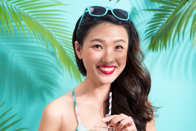 Young asian woman drinks  juice from glass over colorful blue background