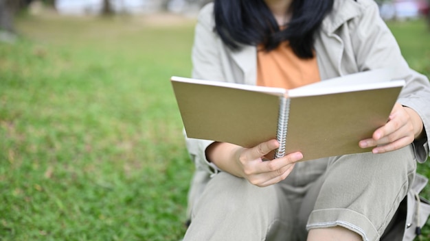 Young Asian woman enjoying reading her novel or book while relaxing in the green park