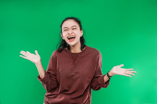 Young Asian woman expressing happy wide-open mouth looking to the camera while causing the palms to rise open on green background