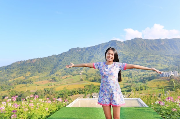 Young Asian woman feeling free with arms wide open at beautiful trees and mountains.