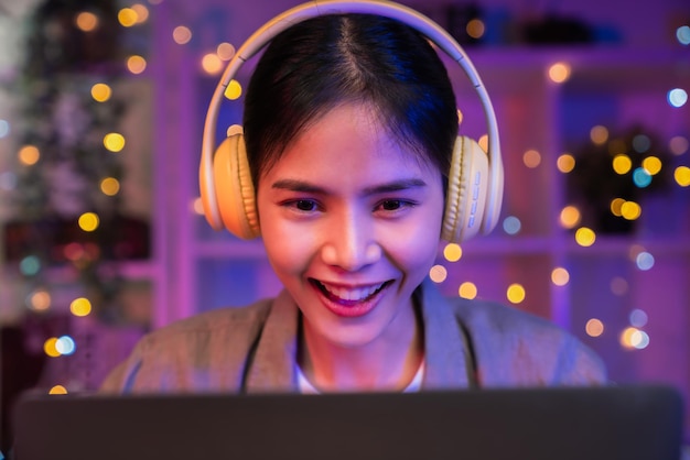 Young Asian woman of happy smiling is listening to music from yellow headphones and hands using laptop on vacation in the house