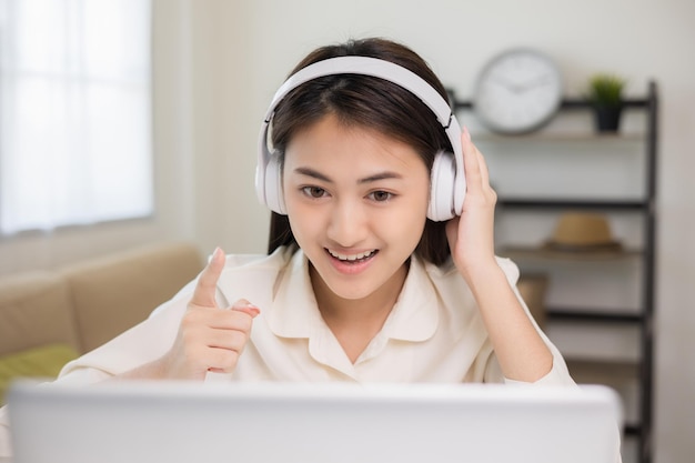 Young asian woman in headphone using laptop chatting video conference online sitting in living room at home Business Woman look at screen Meeting on social live steam Work learning from home