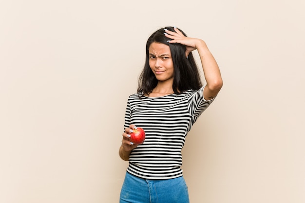 Young asian woman holding an apple being shocked, she has remembered important meeting.