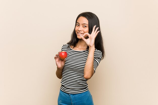 Young asian woman holding an apple cheerful and confident showing ok gesture.