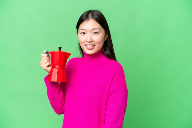 Young Asian woman holding coffee pot over isolated chroma key background smiling a lot