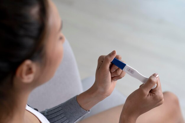 Young Asian woman holding home pregnancy test and looking happy in living room