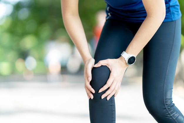 Young asian woman holding knee pain in running public nature park 