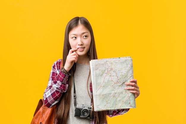 Young asian woman holding a map relaxed thinking about something