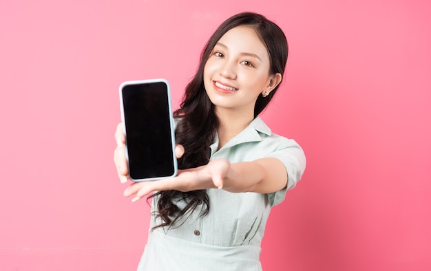 Young Asian woman holding phone in hand and holding it forward on pink