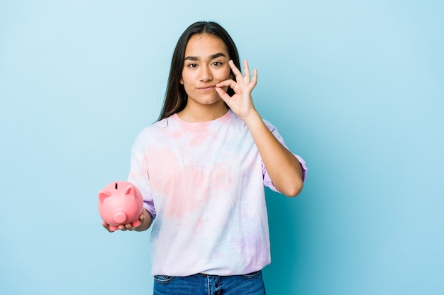 Young asian woman holding a pink bank with fingers on lips keeping a secret.