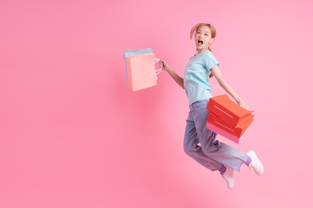 Young Asian woman holding shopping bag on pink background