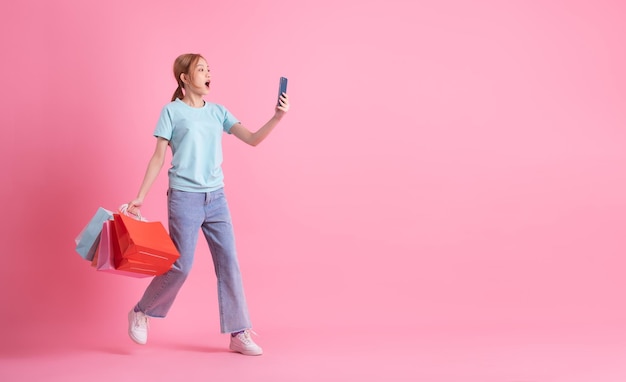 Young Asian woman holding shopping bag on pink background