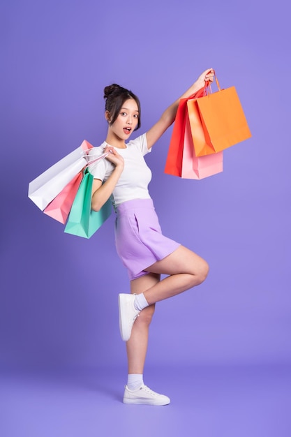 Young Asian woman holding shopping bag on purple background