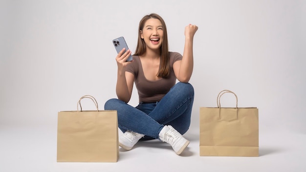 Young asian woman holding smartphone and shopping bag over white background