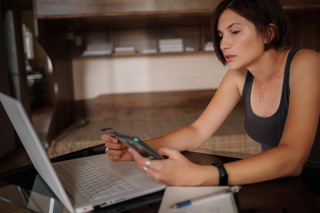 A young asian woman holds a credit card and uses a laptop