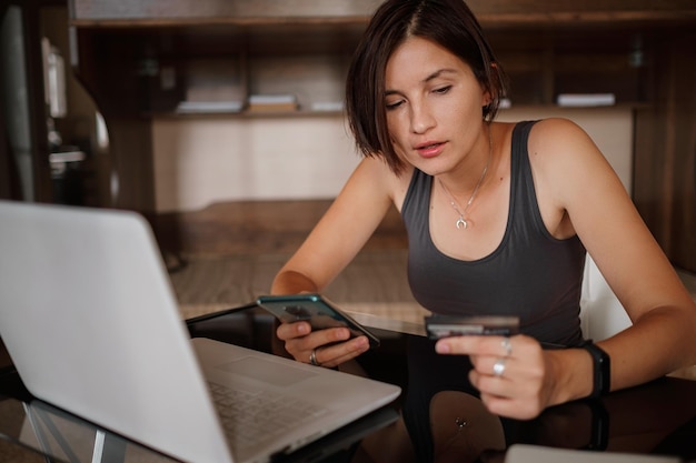 A young asian woman holds a credit card and uses a laptop