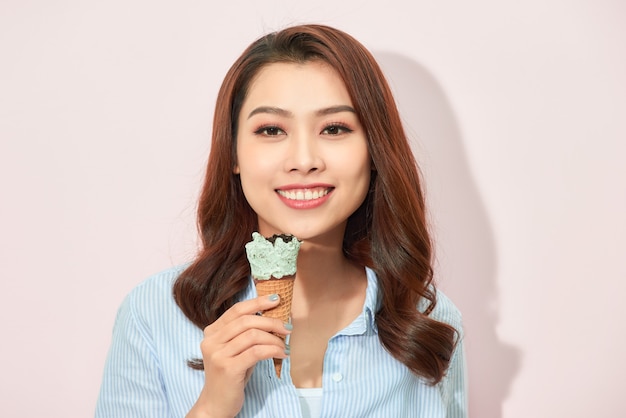 Young asian woman holds tasty ice cream, stands on light pink background