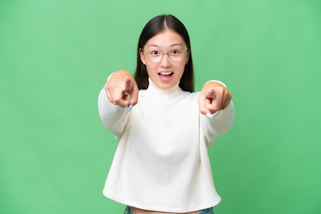 Young Asian woman over isolated background surprised and pointing up