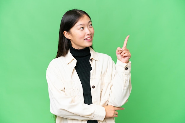 Young Asian woman over isolated chroma key background pointing up a great idea