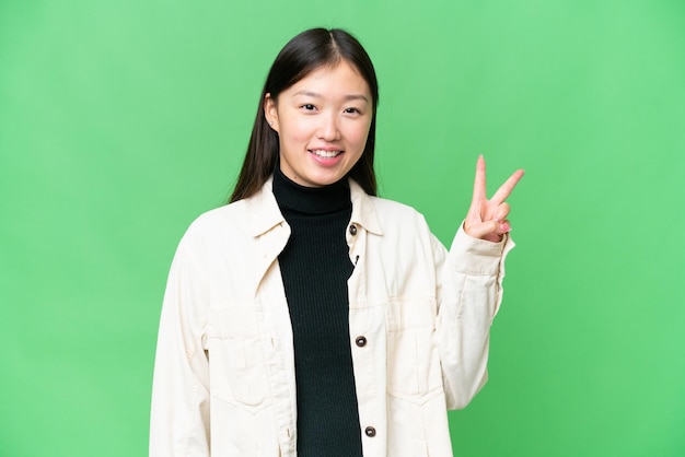 Young Asian woman over isolated chroma key background smiling and showing victory sign