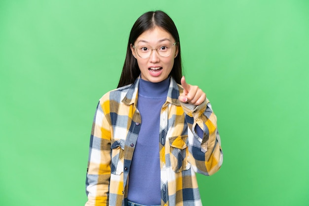 Young Asian woman over isolated chroma key background surprised and pointing front