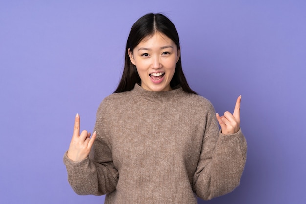 Young asian woman isolated on purple background making horn gesture