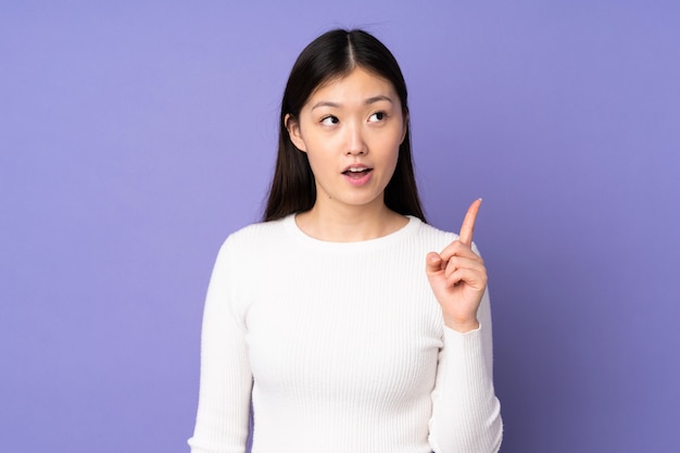 Young asian woman isolated on purple space thinking an idea pointing the finger up