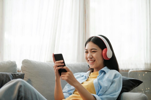 Young asian woman listening to music using smartphone at home