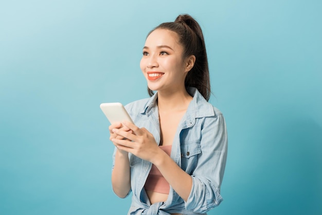 Young Asian woman looking and texting On smartphone While Standing Over yellow Studio Background