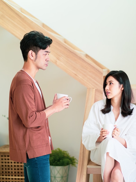 Young asian woman and man are enjoying spending time together at home with cup of coffee in hands.