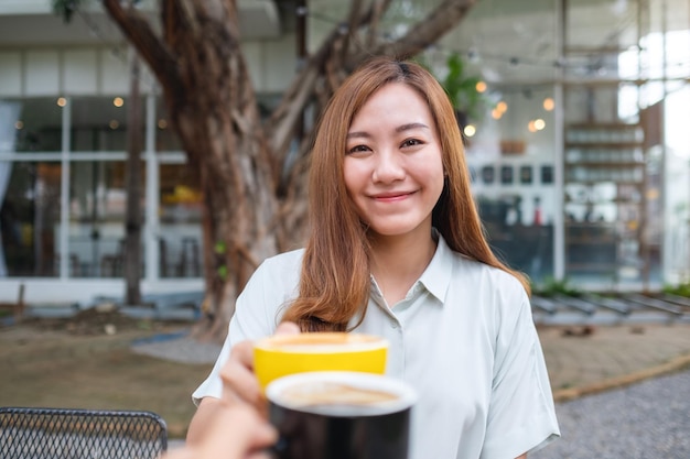 A young asian woman and a man clinking coffee cups together in cafe