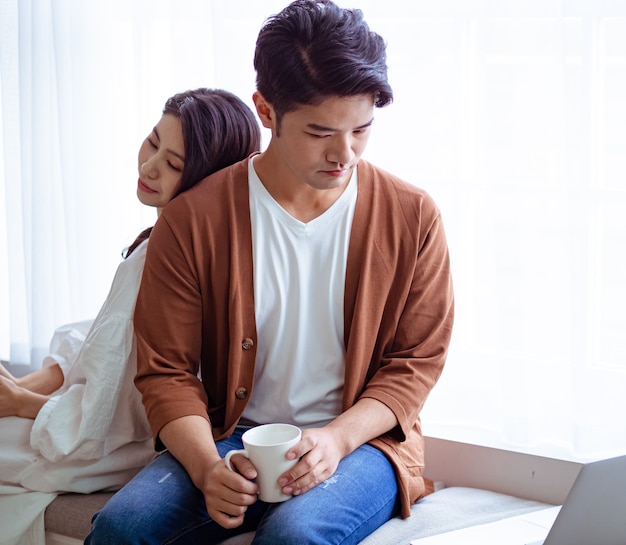 Young asian woman and man at home with cup of coffee in hands.