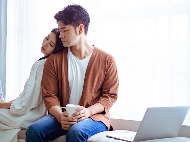 Young asian woman and man at home with cup of coffee in hands.