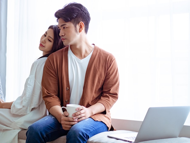 Young asian woman and man at home with cup of coffee in hands.