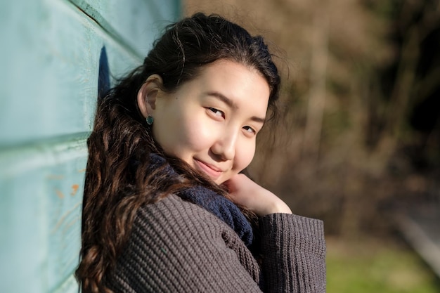 Young asian woman outdoor wearing warm jacket standing near wooden blue wall in sunny autumn day