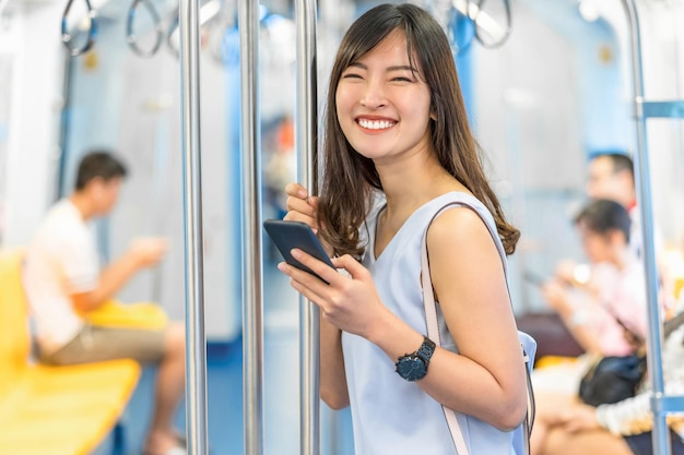 Young Asian woman passenger using social network via smart mobile phone in subway train