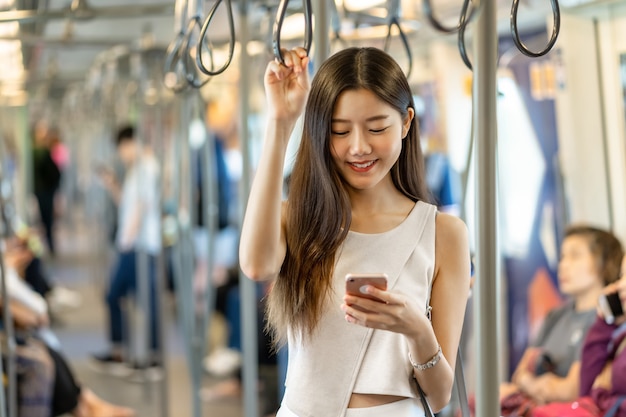 Young Asian woman passenger using social network via smart mobile phone in subway